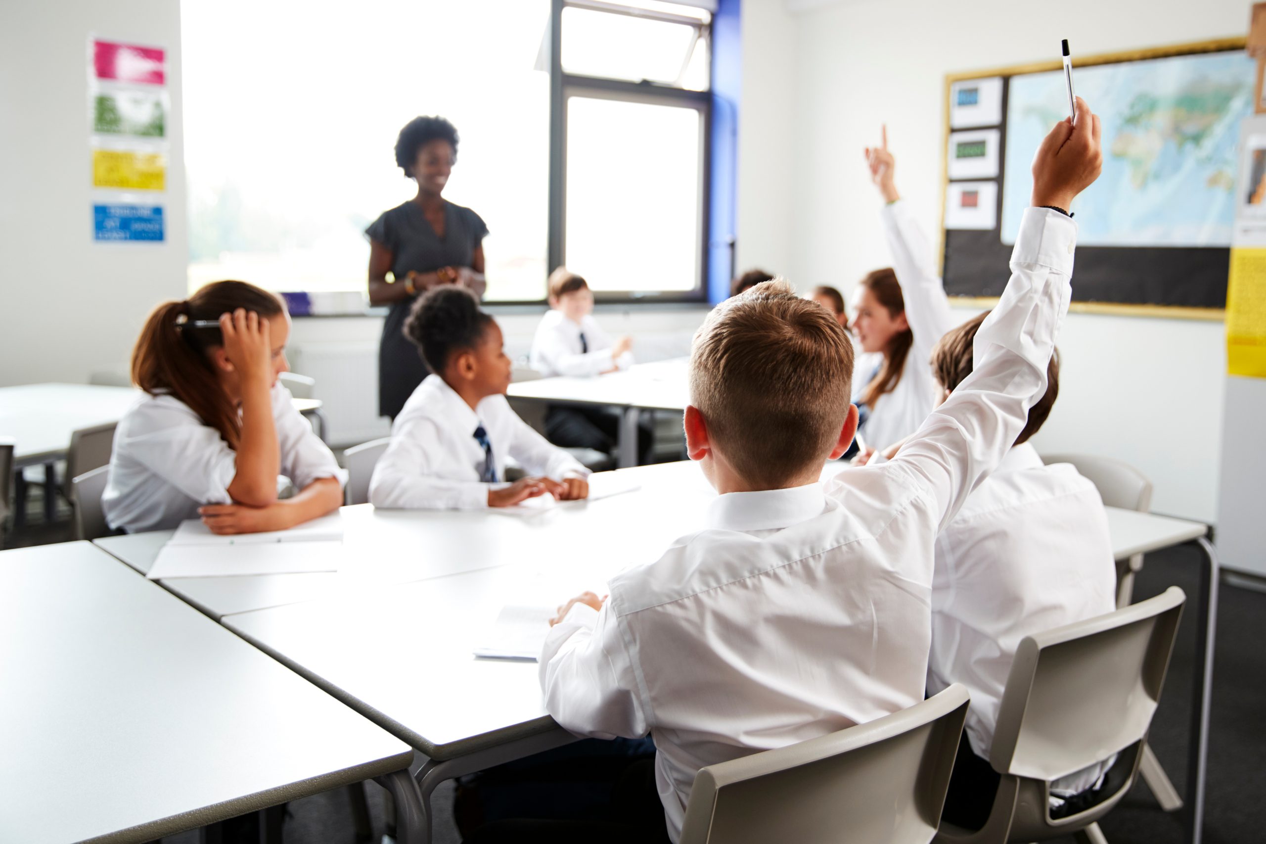 A classroom full of students wearing uniforms. One student is raising his hand to answer a question.