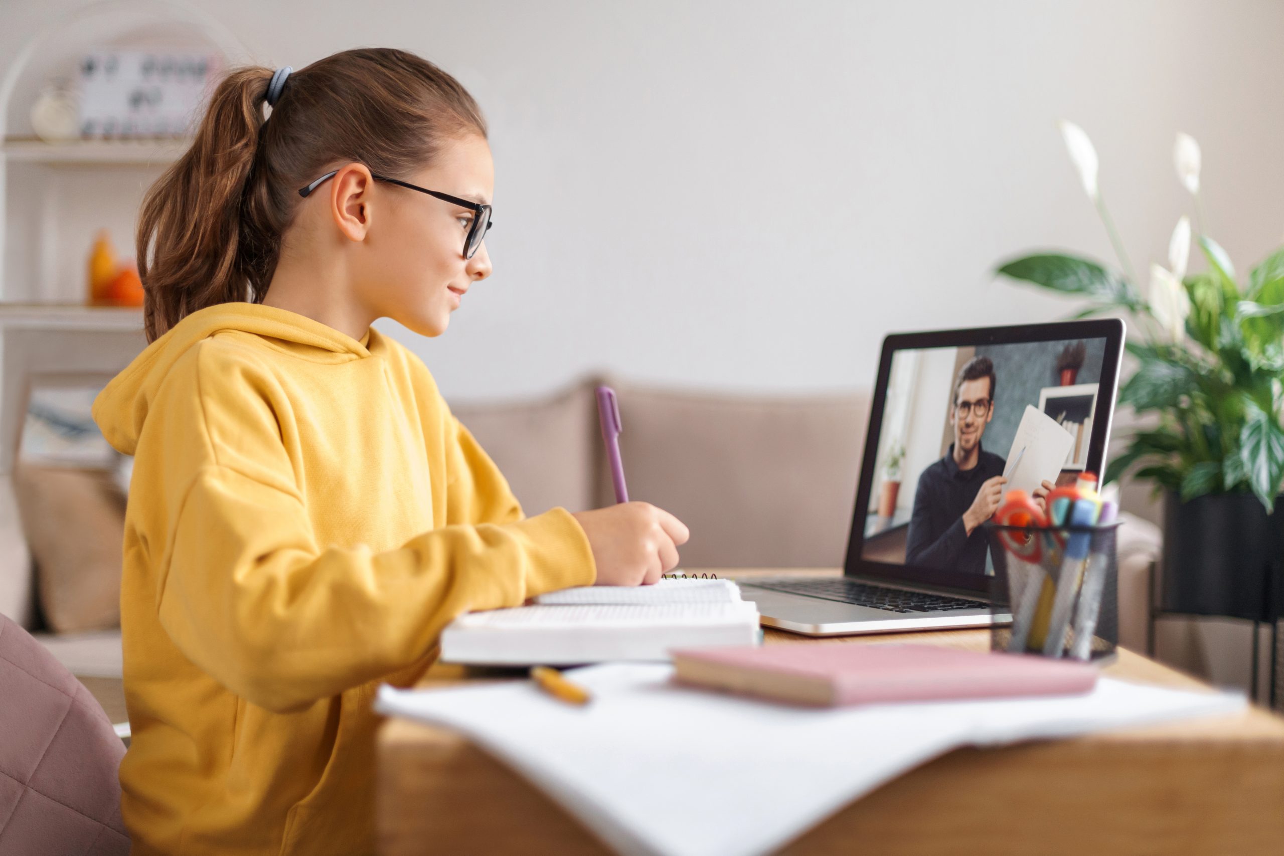 Young female student listening to a virtual lesson taking notes. 