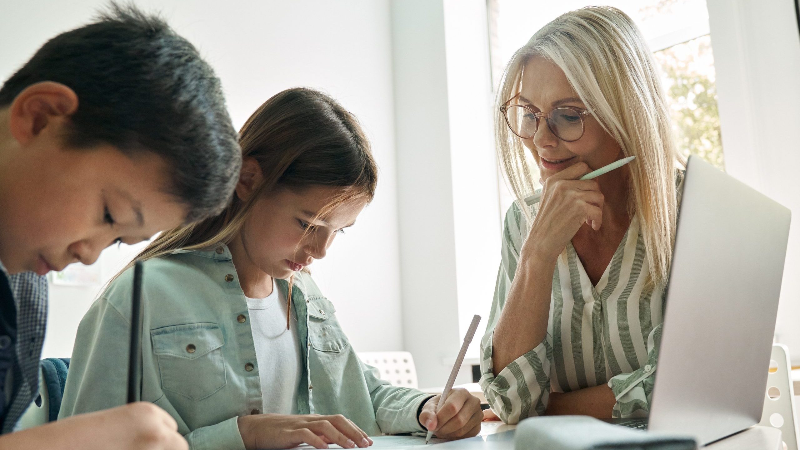 Female teacher or tutor helping students with homework in an at-home setting.