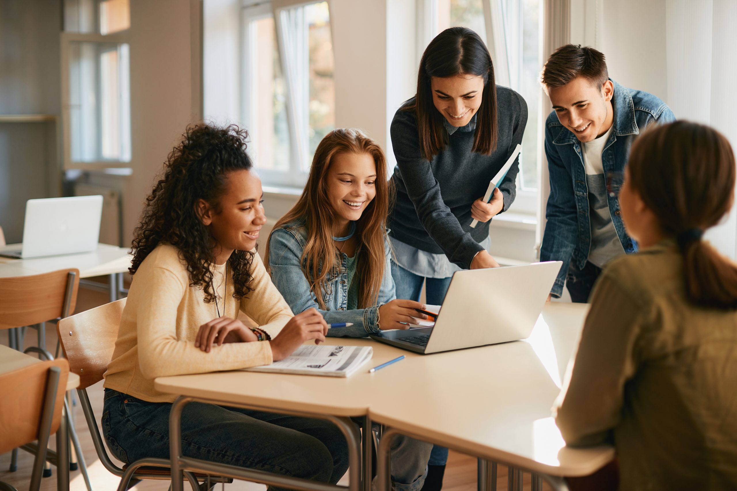 Group of teenage students surrounding a computer in a classroom at a public school.