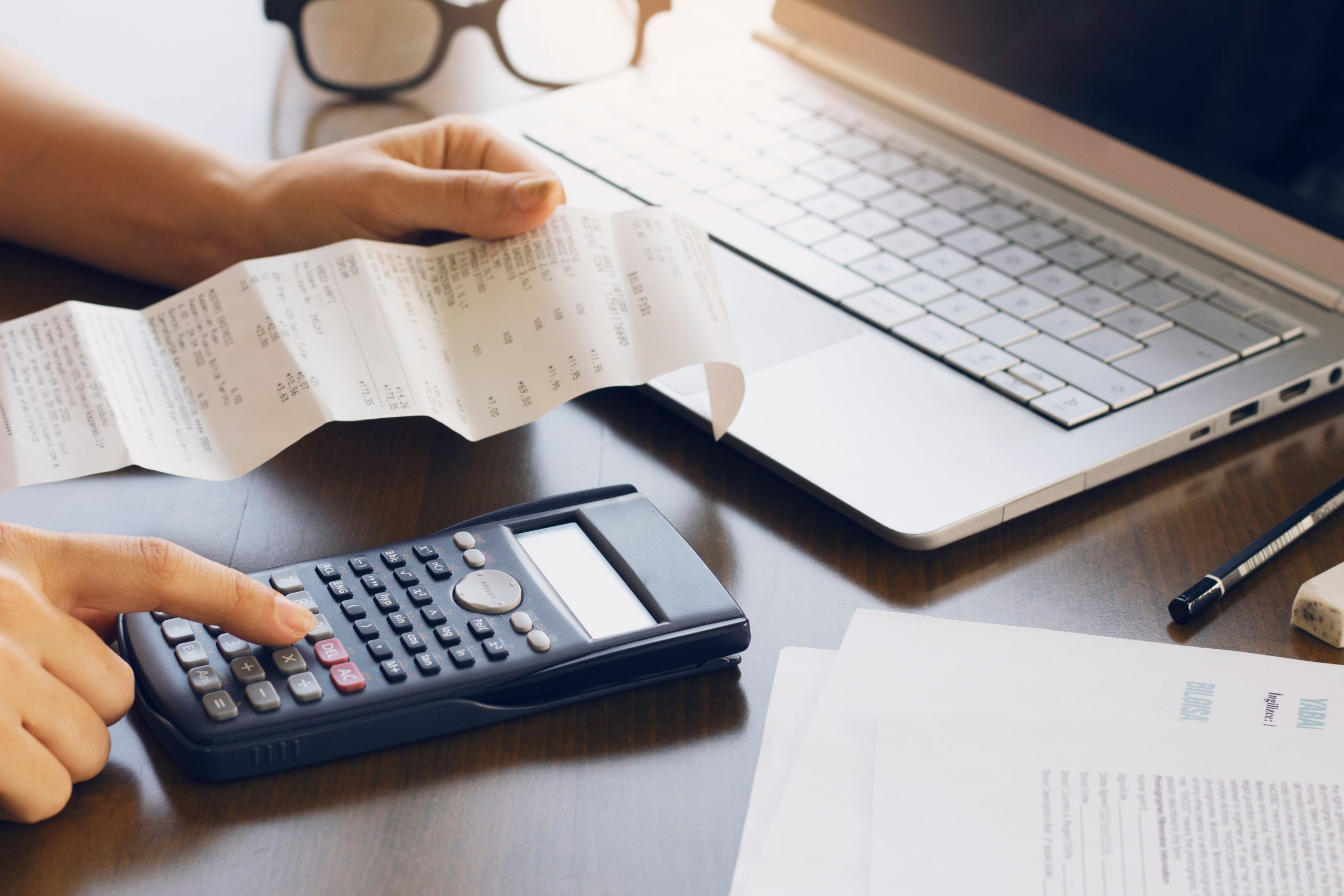 Someone holding a receipt next to a calculator and laptop.