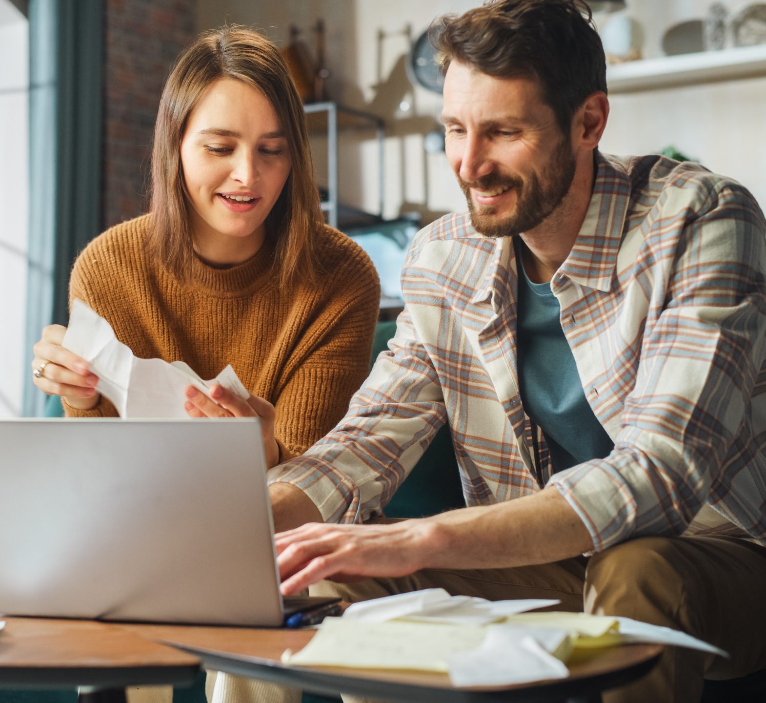 Parents doing accounting at home on a computer and holding paper documents. 
