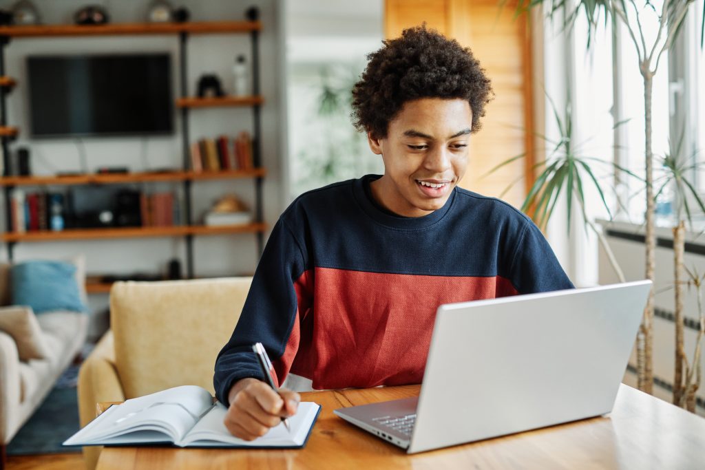 Student writing in a notebook while looking at a computer. 